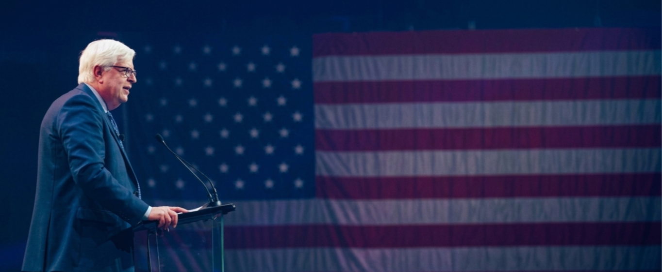 Dennis Prager speech at podium with flag